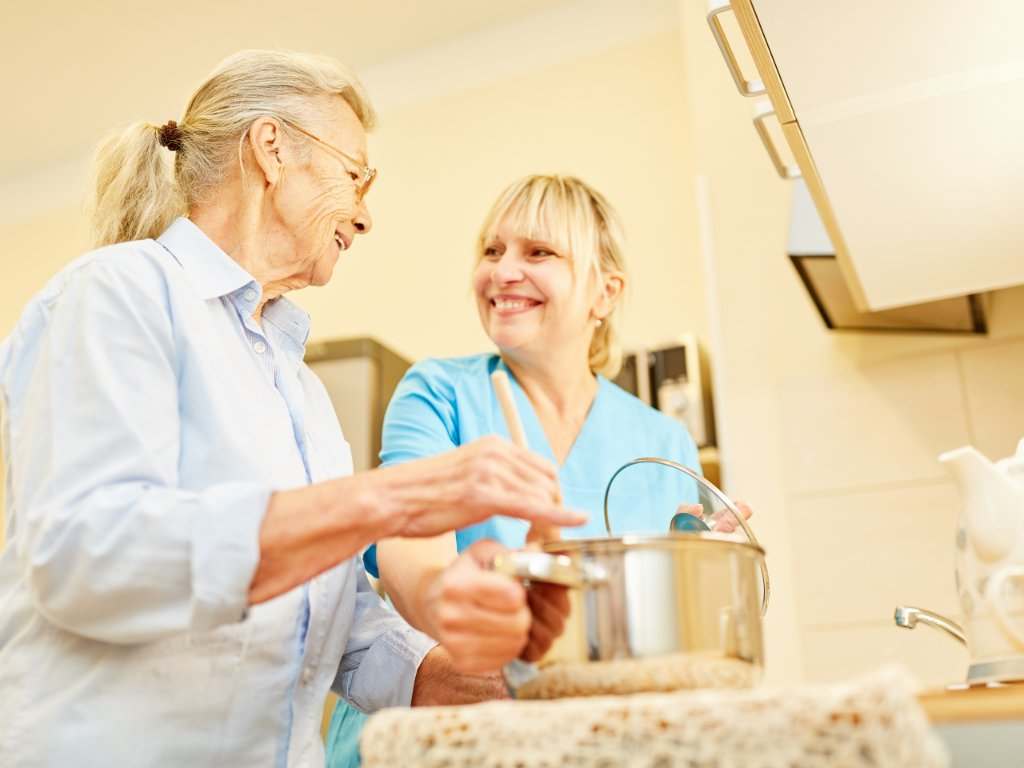Enfermera cocinando con mujer mayor en residencia